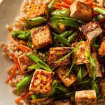 Close-up of Vegan Honey Garlic "Salmon" on a white plate, tofu pieces glazed with sesame seeds and green onions.